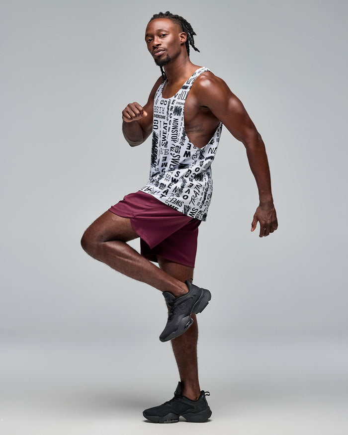 White graphic-print athletic tank with a scoop neckline and deep-cut armholes, shown full length on a male model wearing burgundy athletic shorts and black sneakers in a dynamic pose.