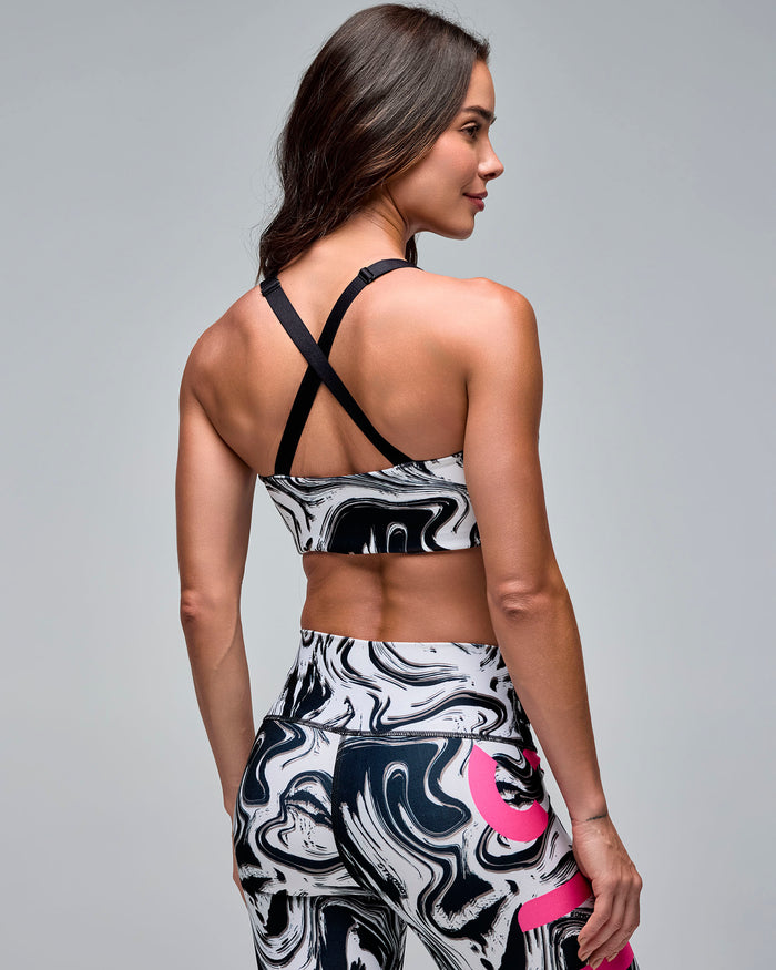 Black, white, and gray marble-print sports bra with adjustable black crisscross straps, shown from the back on a female model wearing matching high-waisted leggings with pink accents.