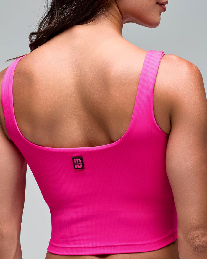 Pink cropped athletic tank with wide shoulder straps and a scoop back, shown in a close-up back view on a female model against a light gray studio background.