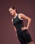 Black sleeveless athletic tank with white trim, shown on a female model wearing black fitted biker shorts against a dark mauve studio background.