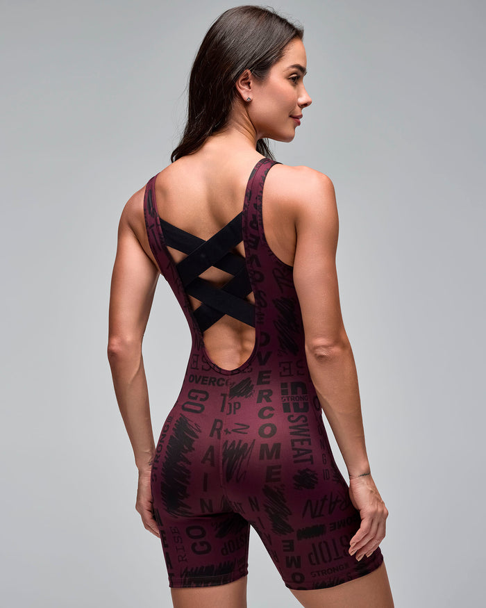 Back view of a burgundy fitted short bodysuit with an allover black motivational word print. Female model wears the sleeveless one-piece with a low back and black crisscross straps against a light gray background.