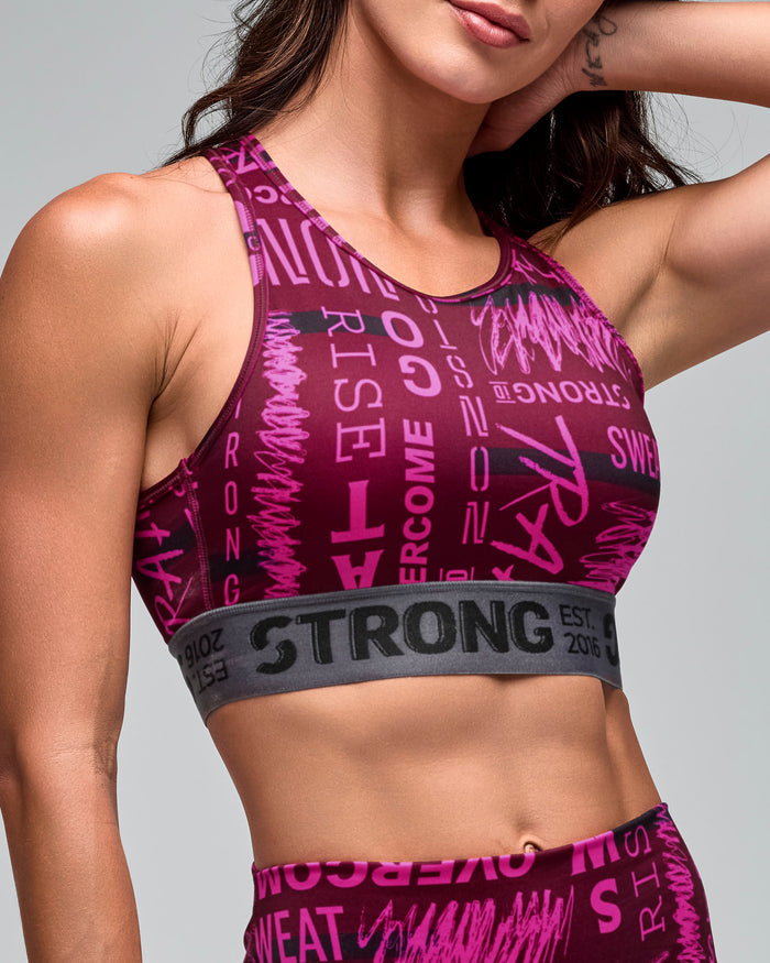 Burgundy and pink graphic-print sports bra with a gray elastic under-band, shown in a close-up on a female model with matching high-waisted leggings against a light gray studio background.
