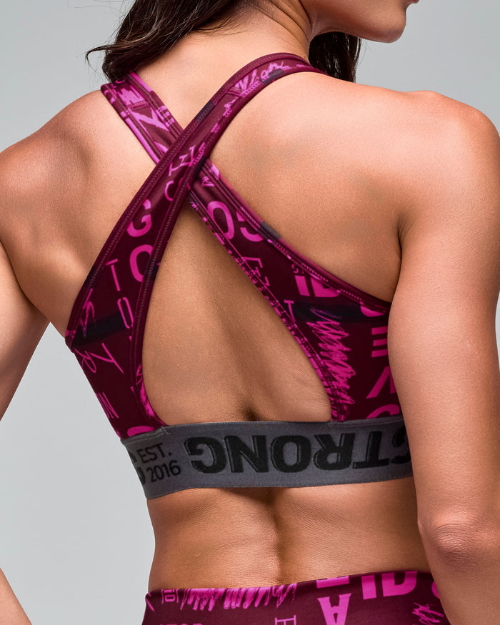 Close up back view of the burgundy and pink graphic-print sports bra with crisscross back straps and a gray elastic under-band, on a female model.