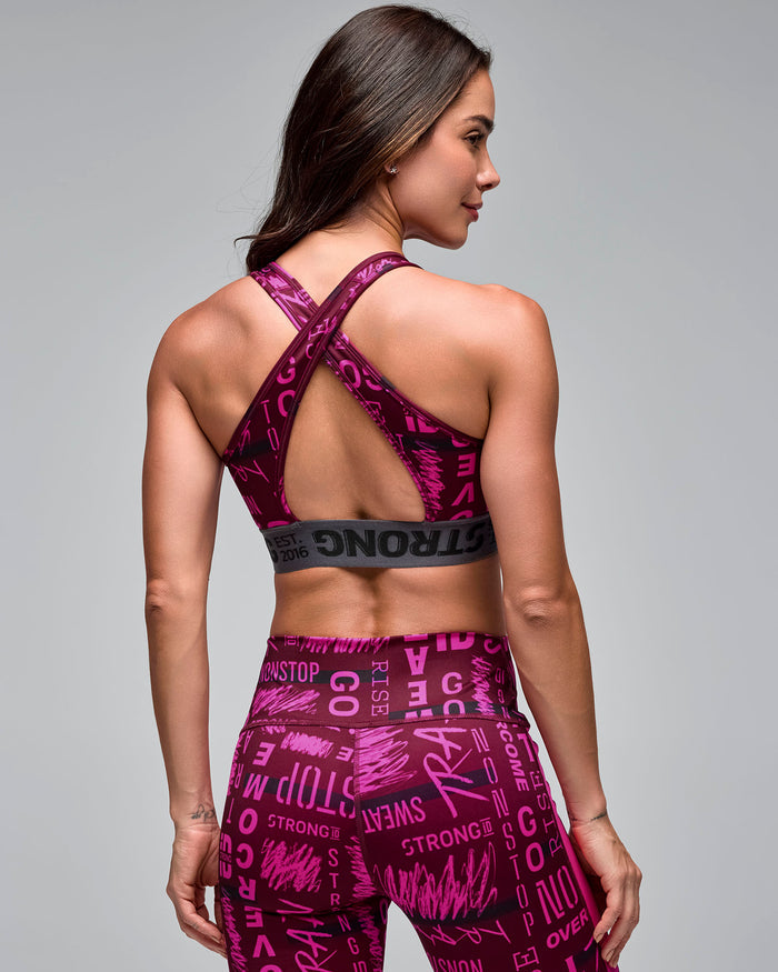 Burgundy and pink graphic-print sports bra with crisscross back straps and a gray elastic under-band, shown from the back on a female model wearing matching high-waisted leggings.