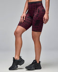 Burgundy high-waisted biker shorts with an allover black motivational word print. Female model wears the fitted mid-thigh shorts with black athletic sneakers in a side view against a light gray background.