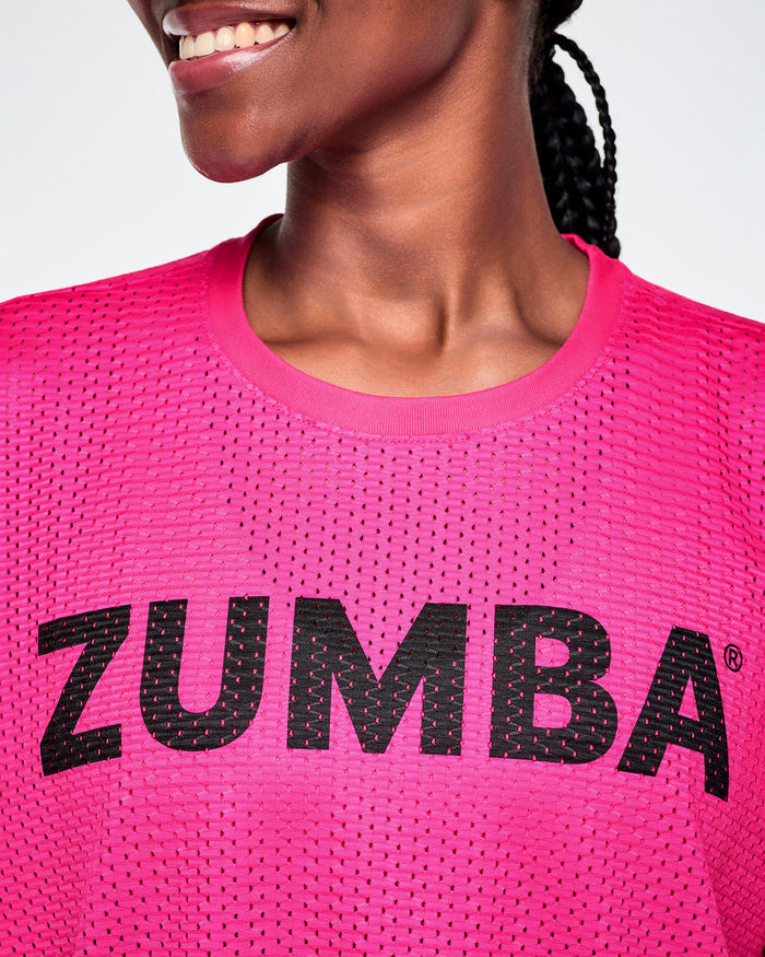 Close-up of a female model wearing a bright pink Zumba mesh top with a black ZUMBA lettering across the chest.