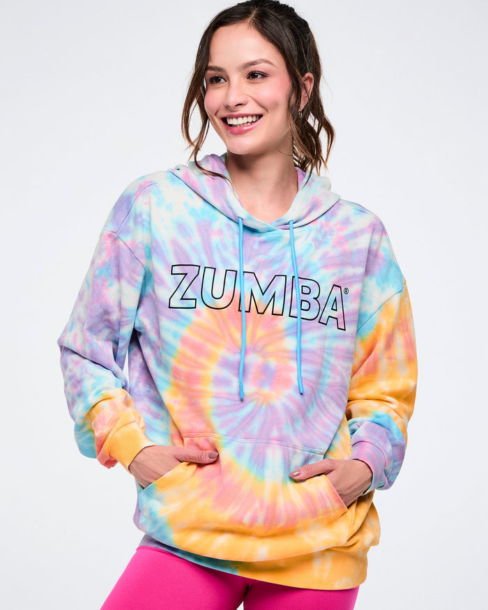 Female model wearing a tie-dye Zumba hoodie with a black outlined Zumba on the chest against a white background.