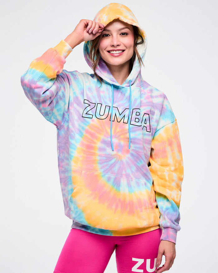 Female model wearing a tie-dye Zumba hoodie showing the hood up, with a black outlined Zumba on the chest against a white background.