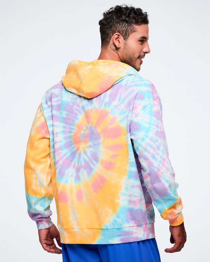 Back view of a male model wearing a colorful tie-dye hoodie and blue pants.