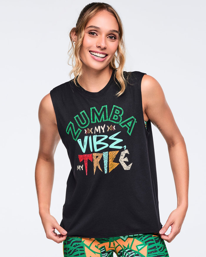 Black sleeveless Zumba graphic tank top with a crew neckline and relaxed fit, featuring colorful “Zumba My Vibe, My Tribe” lettering on the front. Female model wears the top with green, orange, and black abstract print leggings.