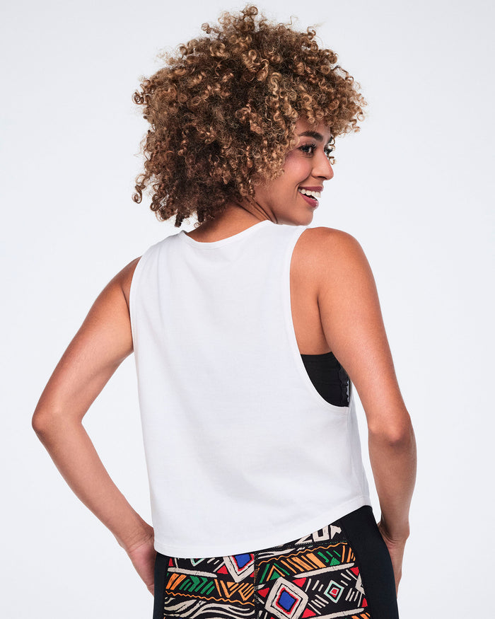 Female model wearing a white sleeveless tank shown from the back with a relaxed fit and deep armholes, paired with black leggings featuring a multicolor geometric print and black side panels.