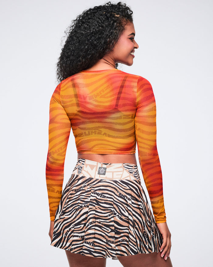 Back view of an orange and red zebra-print sheer long-sleeve crop top with a crew neckline and fitted silhouette. Female model wears the top with a beige, black, and cream zebra-print flared mini skirt.