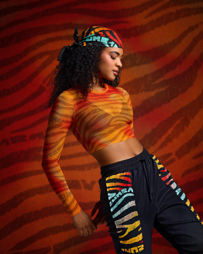Orange mesh crop top on female model with black multicolor joggers and matching bandana against a red zebra backdrop.