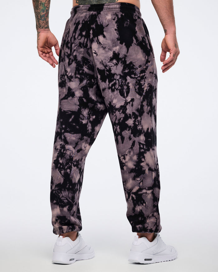 Black and tan tie-dye sweatpants shown from the back. Male model wears the relaxed-fit joggers with an elastic waistband, cuffed ankles, and white sneakers.