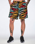 Male model wearing knee-length athletic shorts in a black zebra-stripe print with multicolor brushstroke stripes in yellow, orange, red, mint, and beige, featuring a black drawstring waistband and black low-top sneakers with white soles.