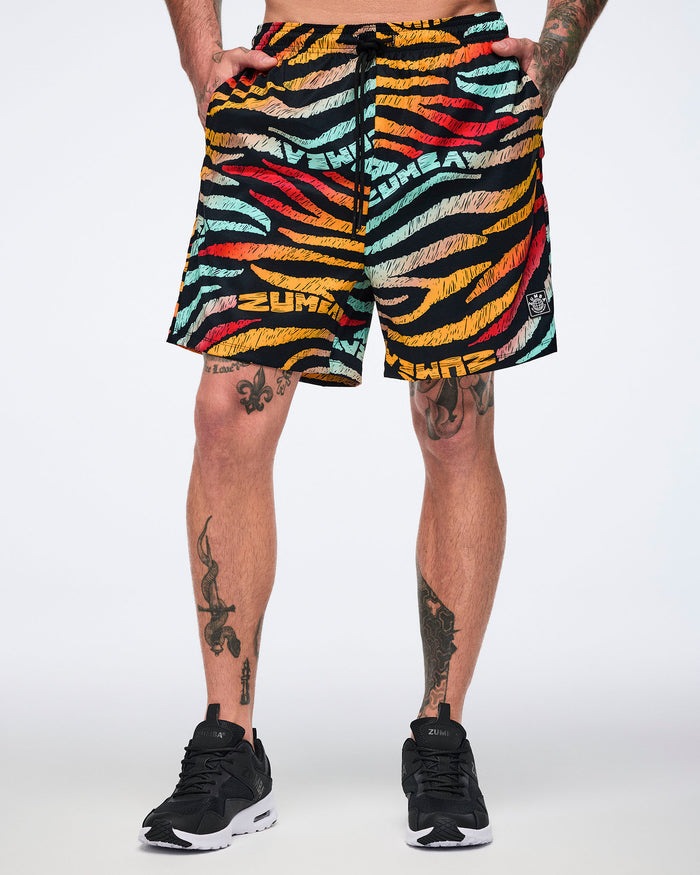 Male model wearing knee-length athletic shorts in a black zebra-stripe print with multicolor brushstroke stripes in yellow, orange, red, mint, and beige, featuring a black drawstring waistband and black low-top sneakers with white soles.