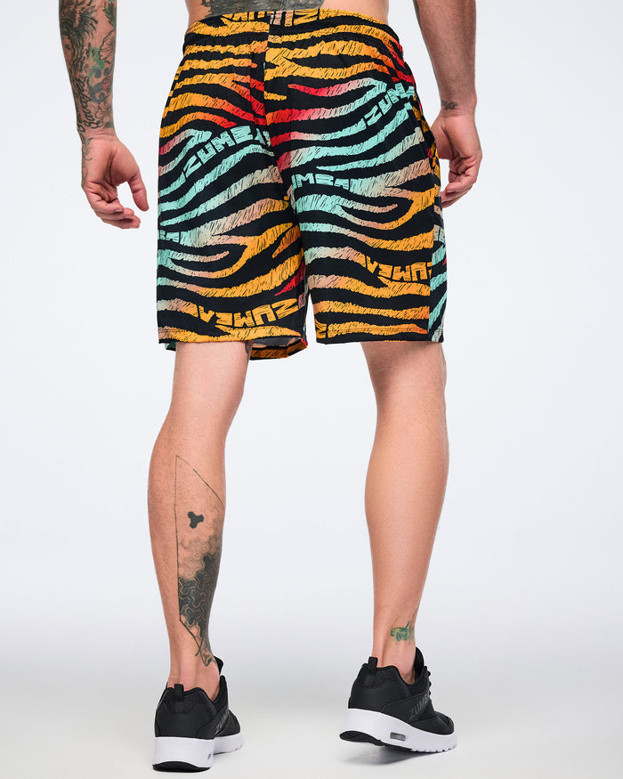 Male model wearing knee-length athletic shorts in a black zebra-stripe print with multicolor brushstroke stripes in yellow, orange, red, mint, and beige, shown from the back with a relaxed fit and black low-top sneakers with white soles.