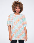 White short-sleeve Zumba oversized T-shirt with a crew neckline and allover mint and orange diagonal logo print. Female model wears the tunic-length tee with black leggings.