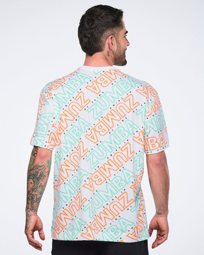 Back view of a white short-sleeve Zumba T-shirt with a crew neckline and allover mint and orange diagonal logo print. Male model wears the relaxed-fit tee with black pants.