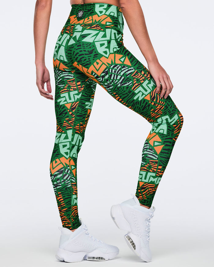 Female model wearing high-waisted full-length leggings in a green, mint, orange, and black abstract print, shown from the back with a body-hugging fit and white high-top sneakers.