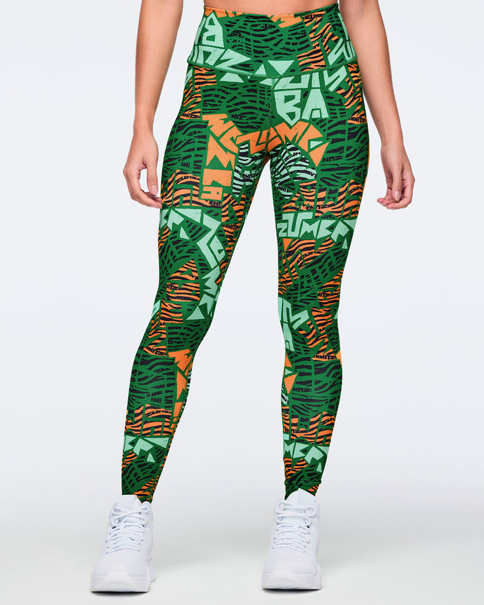 Female model wearing high-waisted full-length leggings in a green, mint, orange, and black abstract print with a wide waistband, full-length fit, and white high-top sneakers.