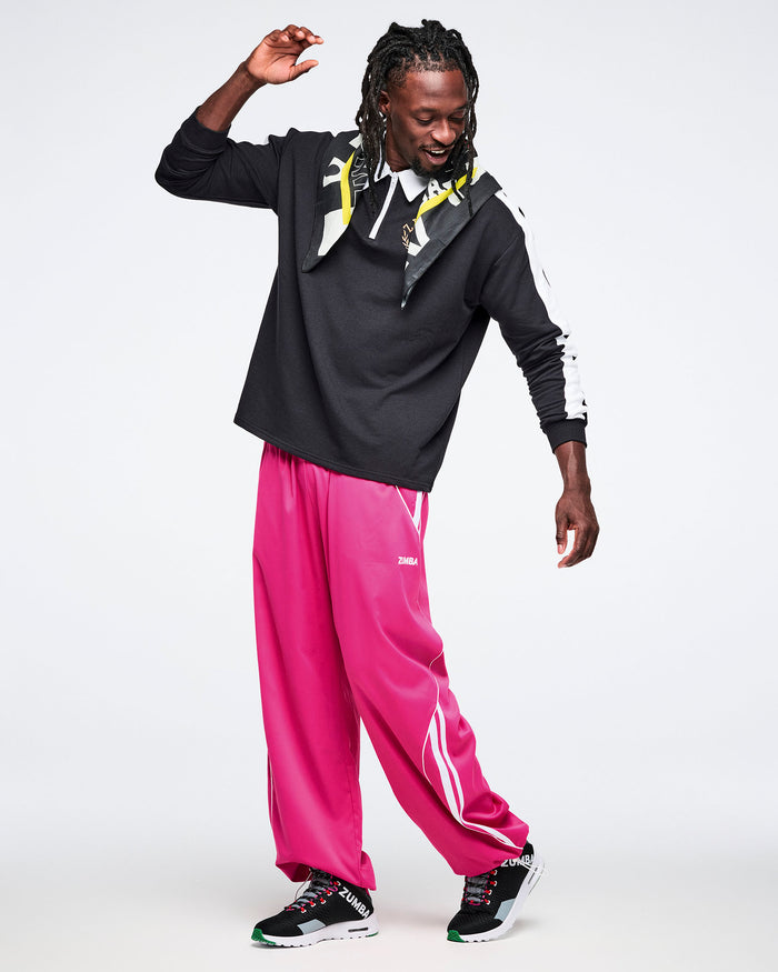 Male model in a black polo with a bandana draped around his neck, pink pants, and black sneakers, set against a white background.