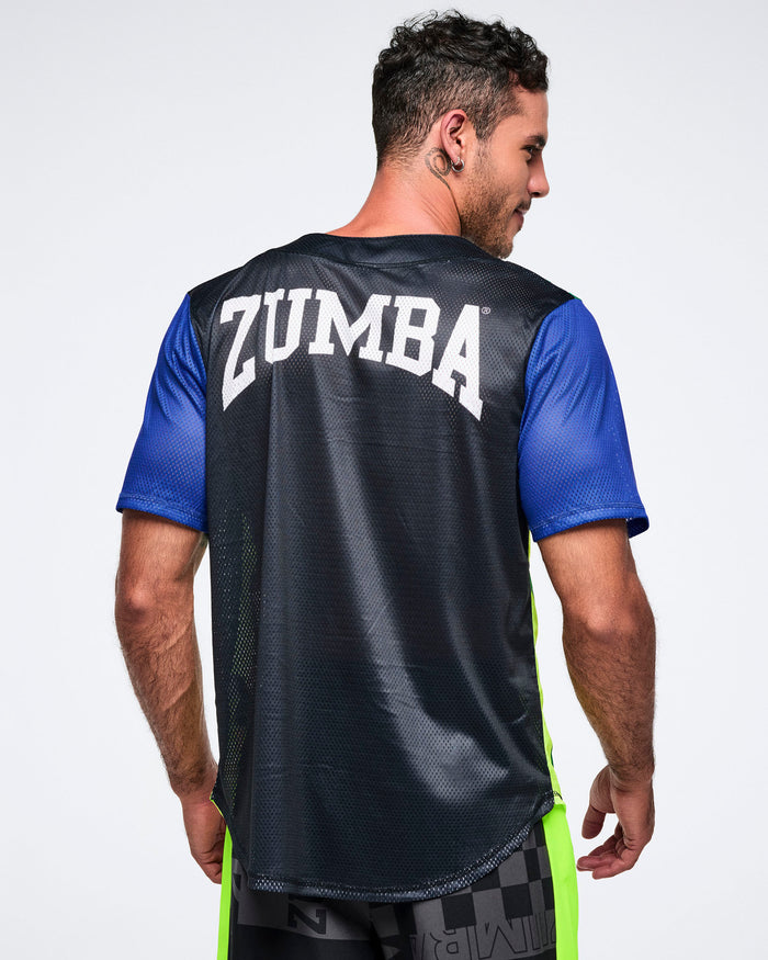 Back view of a male model wearing a black Zumba shirt with blue sleeves with Zumba in white text, on a plain background.