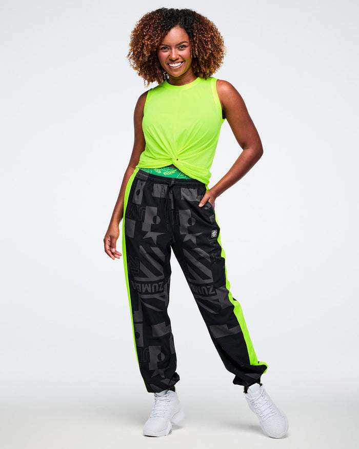 Female model wearing a neon yellow twist sleeveless top and black pants with neon green stripes on the sides against a white background.