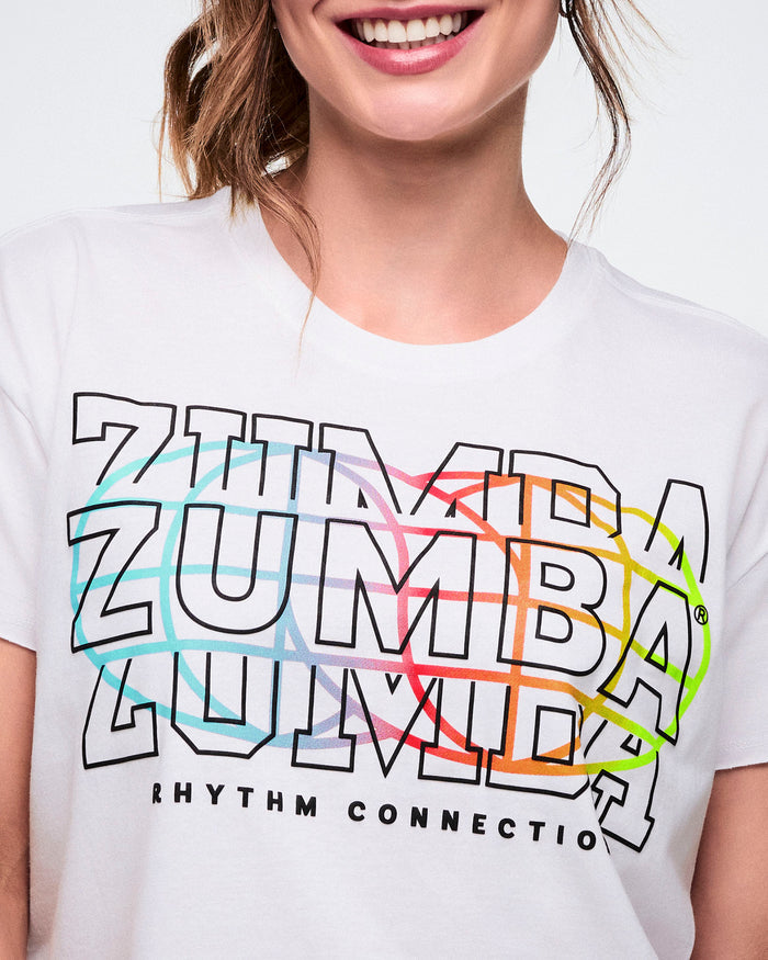 Close-up of a female model in a white Zumba T-shirt with “Zumba” repeated three times, “Rhythm Connection” in black beneath, and a colorful globe icon on the back.