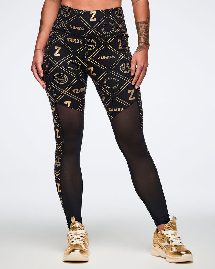 Female model wearing black Zumba leggings with gold patterns, paired with gold shoes on a white background.