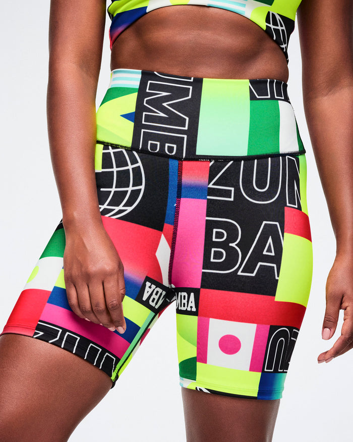 Female model close-up wearing colorful biker shorts with graphic designs on a plain background.