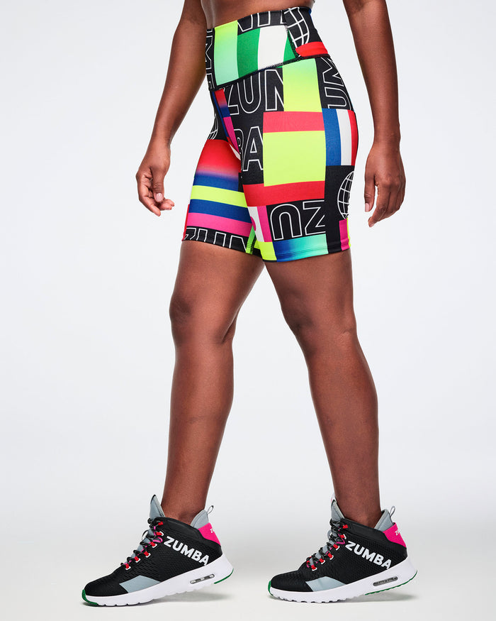 Side view of a female model wearing colorful Zumba shorts and black sneakers on a white background.