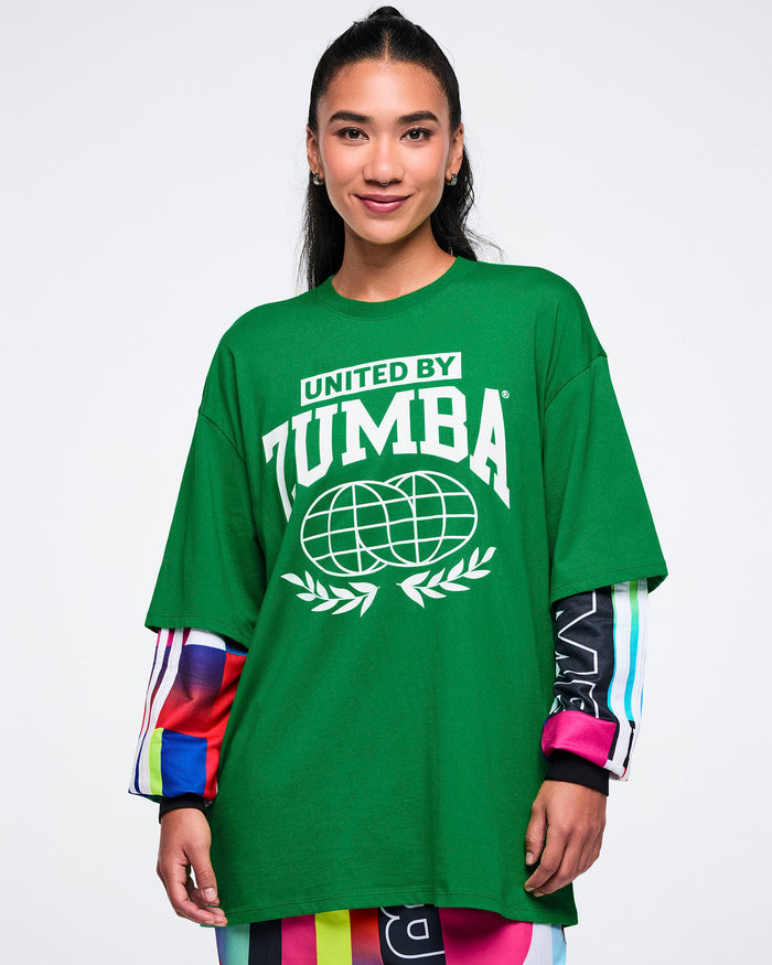 Female model wearing a green 'United by Zumba' t-shirt on a white background.