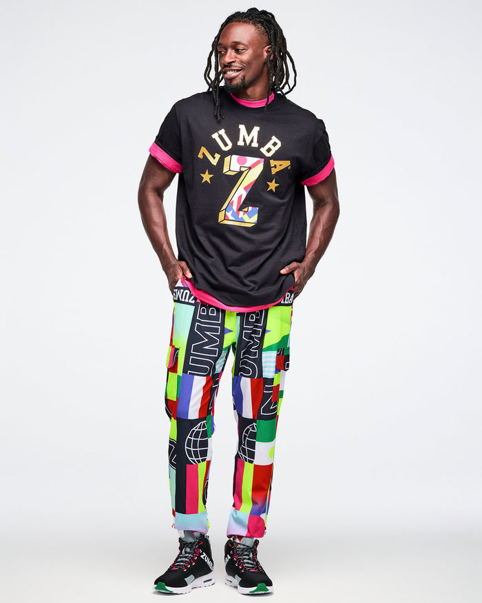 Male model wearing a black t-shirt with colorful graphics and multicolored pants on a white background.