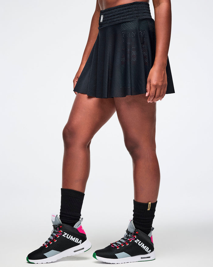 Female model wearing a black Zumba skort, black socks and black and pink shoes on a white background.