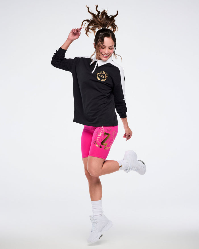 Female model in black polo, pink shorts, white socks and shoes posing on a white background.