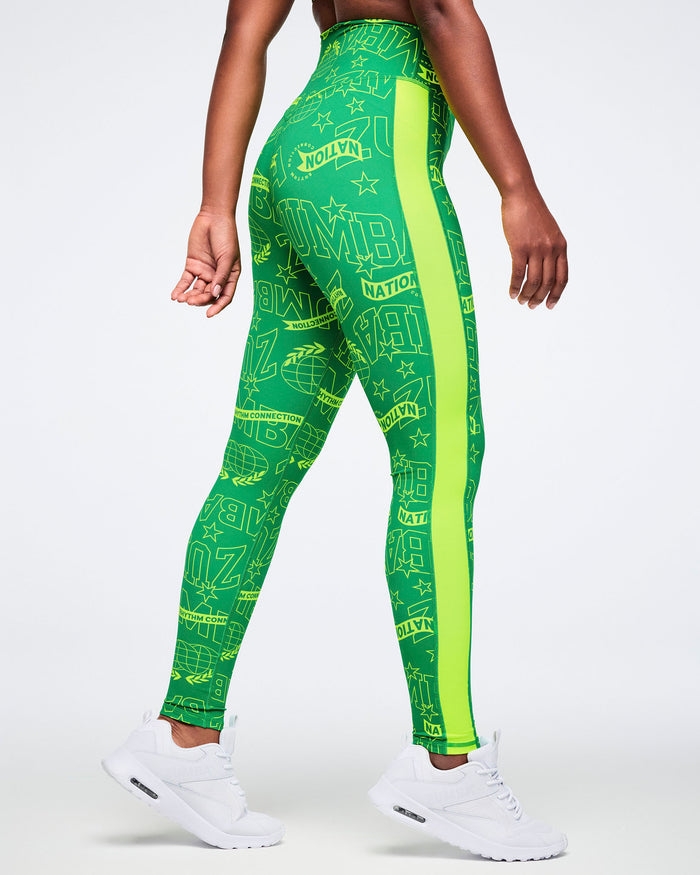 Side view of a female model wearing green leggings with Zumba text and a yellow stripe on a white background.