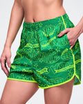 Female model wearing green athletic shorts with neon yellow accents and text on a white background.