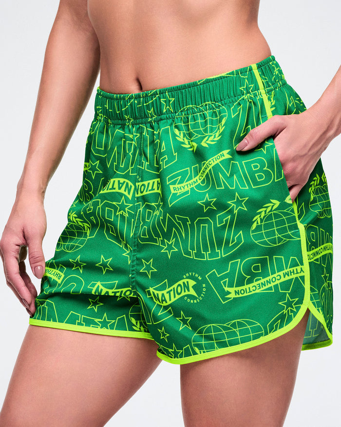 Female model wearing green athletic shorts with neon yellow accents and text on a white background.