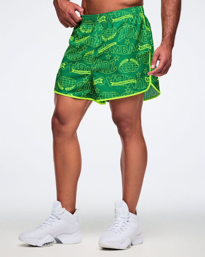 Male model wearing green Zumba shorts with white sneakers on a light gray background.