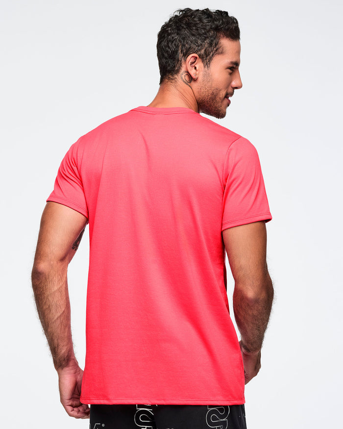Bright coral pink Zumba T-shirt shown from the back with a plain design and classic crew neckline. Male model is turned away and wearing the short-sleeve tee with black graphic pants.