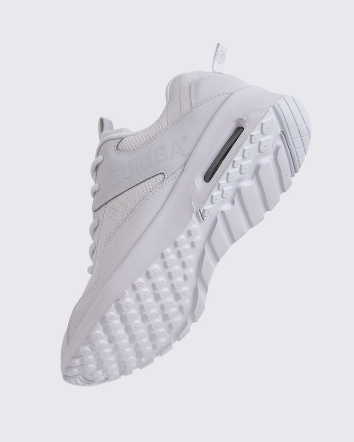 White Zumba low-top athletic sneaker shown from the bottom angle, emphasizing the textured lug outsole, deep grooves, and visible air cushioning in the heel.
