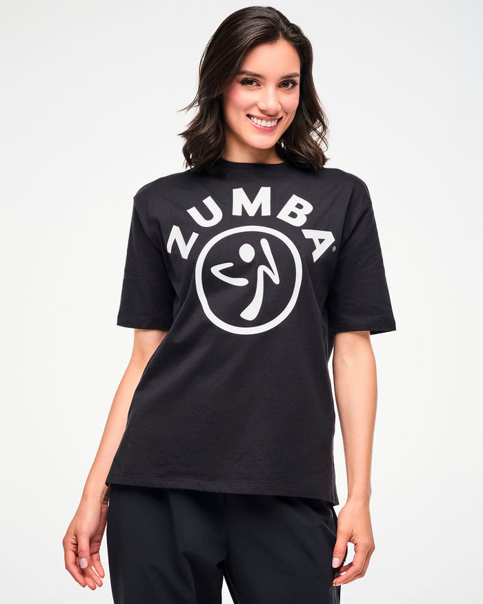 Female model wearing the black oversized T-shirt with white 'ZUMBA' text and a Zumbito logo, paired with black joggers.