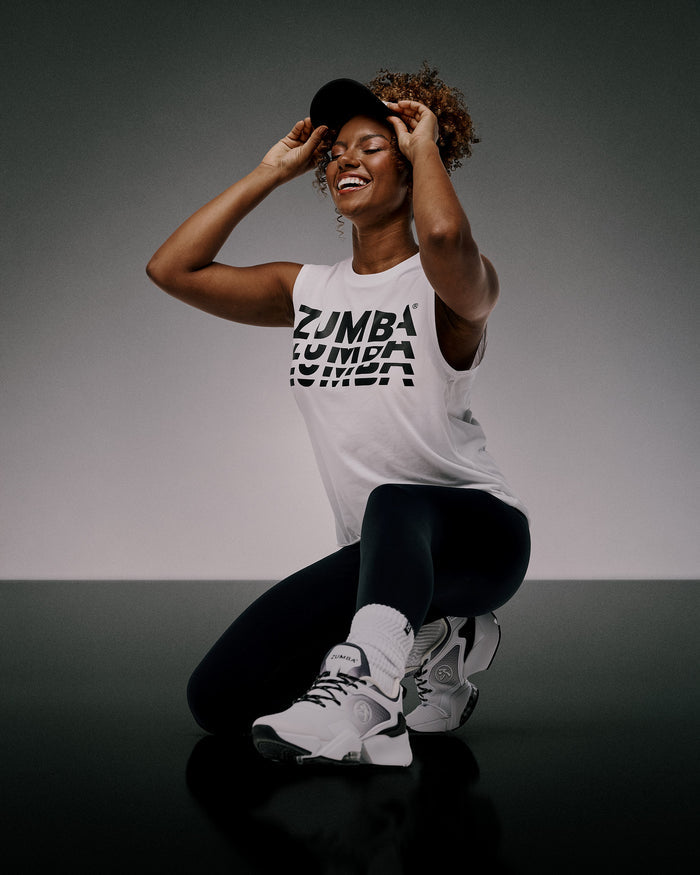 Female model wearing a Zumba tank top and black leggings on a gray background.