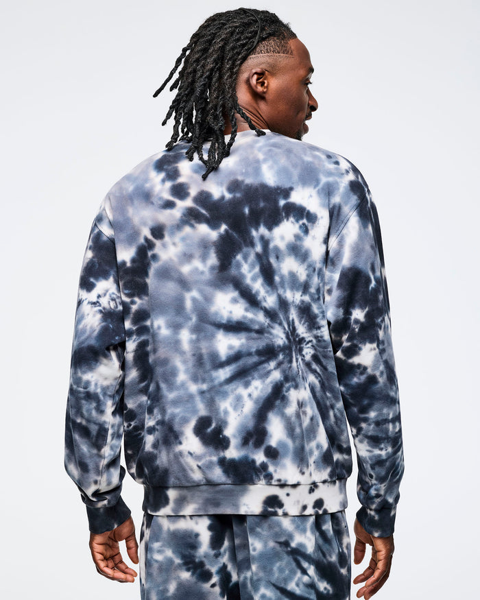 Back view of a male model wearing a Zumba tie-dye sweatshirt on a light gray background.