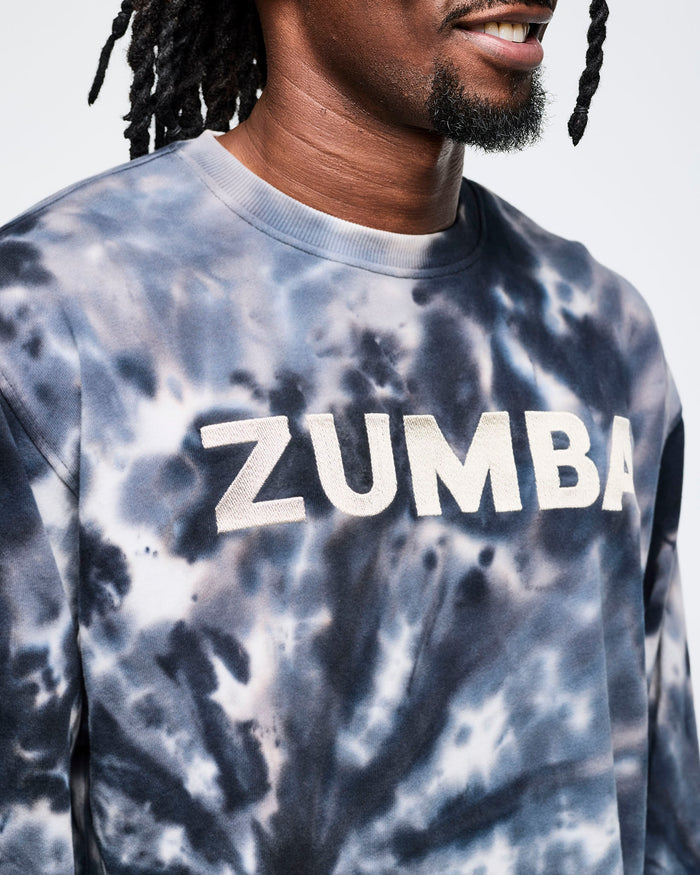 Close-up view of a male model wearing a tie-dye Zumba sweatshirt featuring “ZUMBA” in white across the upper chest.