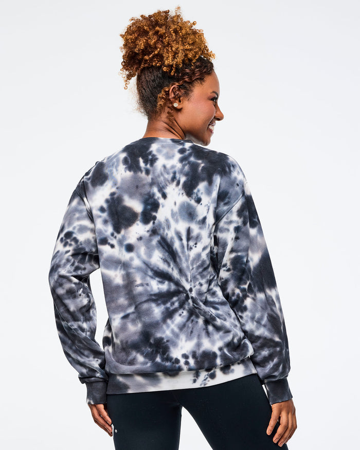 Back view of female model wearing a Zumba tie-dye sweatshirt on a light gray background.