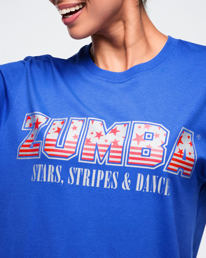 Close-up view of the blue Zumba t-shirt with red‑and‑white stars and stripes, plus “stars, stripes & dance” text below against a white background.