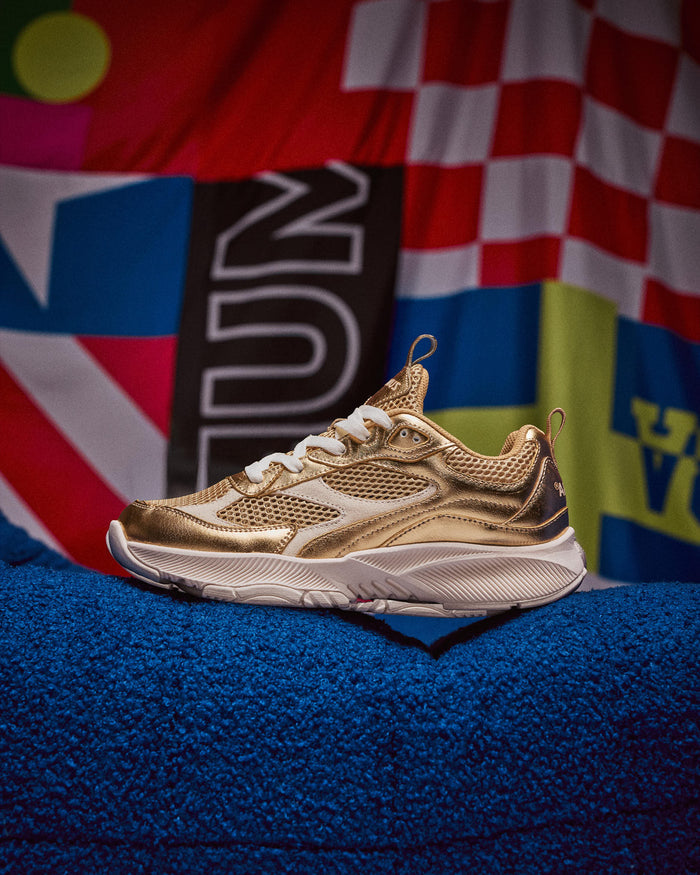 Gold athletic shoe on a blue surface with colorful background.