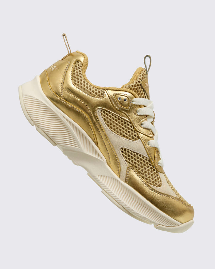 Side angled view of the gold Zumba shoe with laces and back pull tab on a light background.